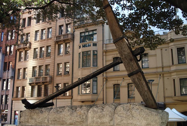 Large ships anchor on stone plinth with stone buildings in the background. 