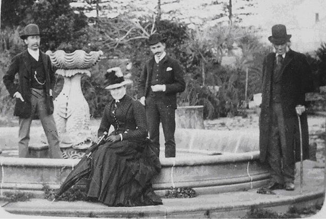 A black-and-white historic photograph of people sitting and standing around and in the John Baptist fountain.