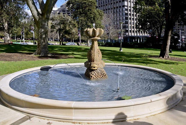 A circular pool with a sandstone rim. A sandstone sculpture of a large fish resting head first on a piece of coral and balancing a clamshell bowl on its tail is in the centre of the pool.