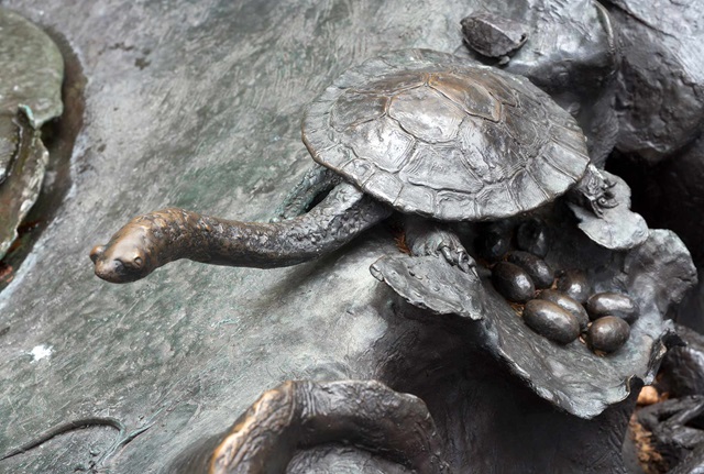 Sculpture of a turtle laying eggs is attached to a larger part of a bronze fountain