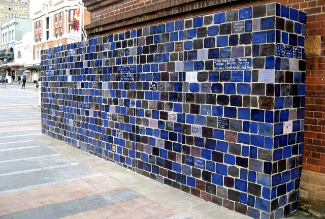 2.4 metre high wall clad in glazed tiles with writing on random tiles
