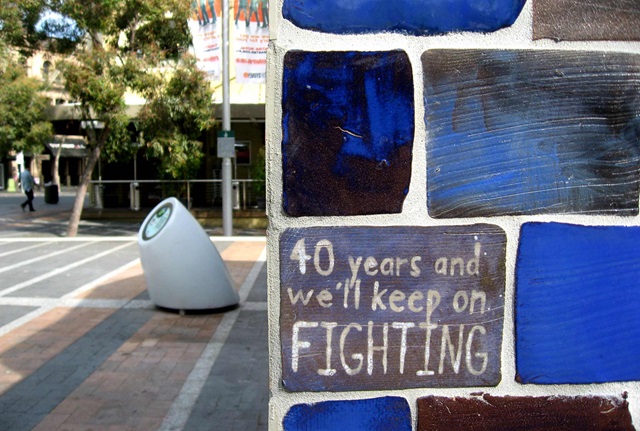 Wall clad in glazed tiles with writing on a tile that reads: 40 years and we'll keep on fighting