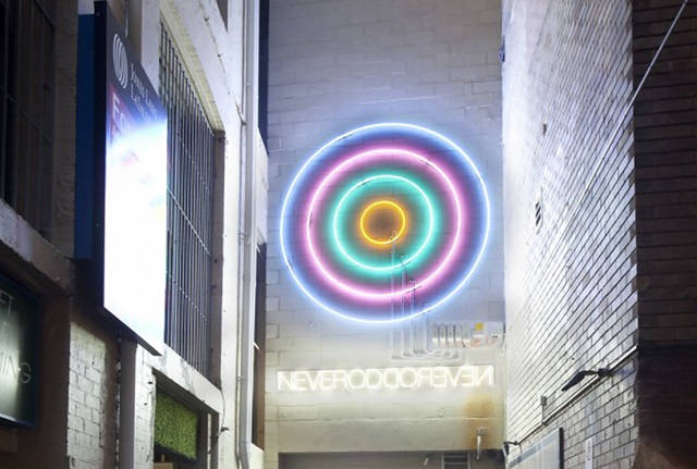 A neon sign of concentric circles, below which is another neon sign reading "NEVERODDOREVEN".