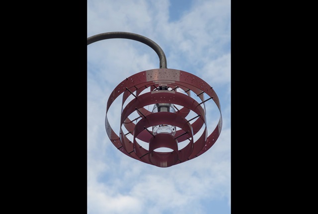 View from below of a pink lampshade on a streetlight. The shade is made of concentric rings of metal.