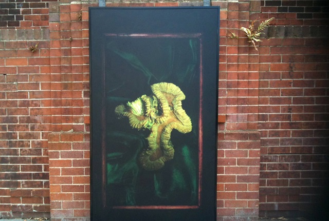 Large rectangular poster image of green coral on a black background affixed to a brick wall