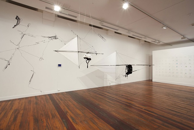 Objects hand from the ceiling of a  white walled studio with wooden floor