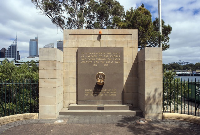 A small rectangular wall made of sandstone blocks. There is a torch attached to the top of the wall, and a large plaque below it commemorates the place of farewell for soldiers who left for the Great War. Two steps lead up to the plaque, and in the middle of it is a brass drinking fountain.