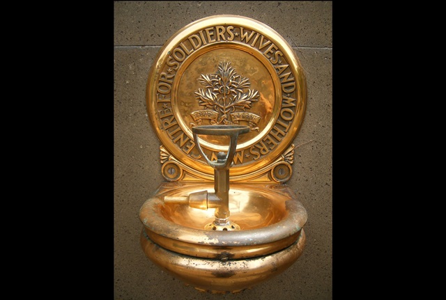 Close view of a brass drinking fountain. Behind the bubbler is a brass plaque featuring a sprig of rosemary for remembrance, and the words "NSW Centre for Soldiers Wives and Mothers"