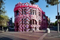 Building painted in fluorescent pink, black and blue geometric diamonds, with the words ‘Always was, always will be‘ is incorporated across the frontage