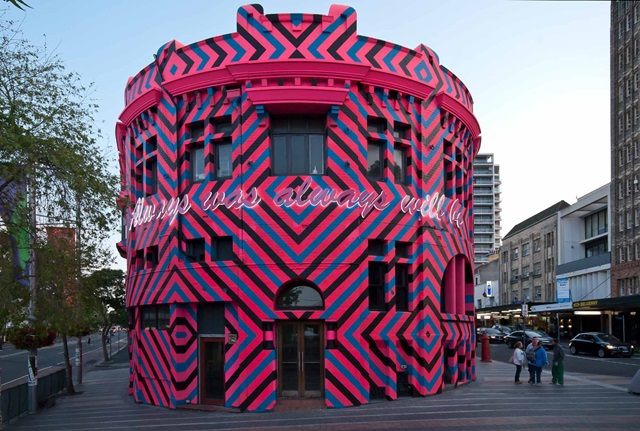 Building painted in fluorescent pink, black and blue geometric diamonds, with the words ‘Always was, always will be‘ is incorporated across the frontage