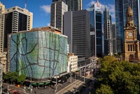 Huge pieces of printed fabric wrap around scaffolding covering the Woolworths building in Sydney, city skyline dominates the background