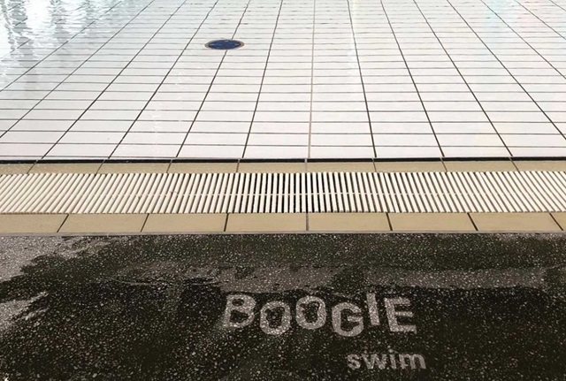 Splashed water on edge of a concrete swimming pool reveals words Boogie swim