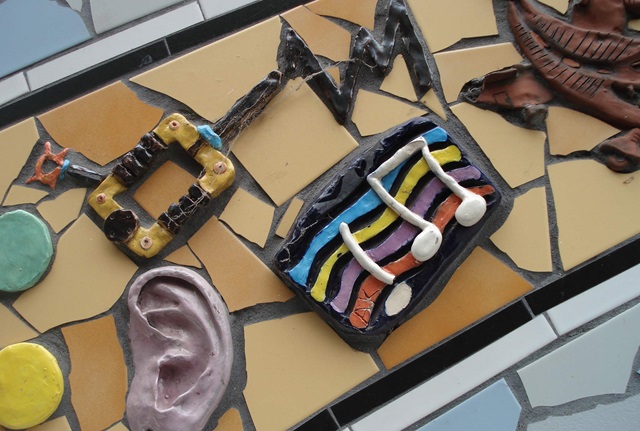 A large mosaic depicting geometric shapes and patterns made from ceramic tiles, with three-dimensional ceramic pieces amongst the tiles.