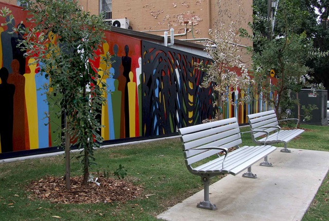 Mural painted on a fence in a park next to a seating area and grass