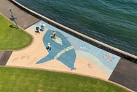 Aerial view of a footpath mural. The mural depicts a beach-like scene, with a very large blue creature and several other much smaller creatures in various colours.