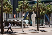 A two-dimensional statue of former Prime Minister, Ben Chifley, made from flat sheets of stainless steel, in the style of a cartoon drawing stands in Chifley Square Sydney surrounded by buildings and palm trees
