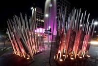 sculpture rising from the ground consisting of a concertina of screens with the pattern of feathers illuminated at night on a street corner