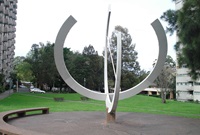 large cement and pebblecrete sundial made of hollow steel and painted white is at the centre of a circular pebblecrete area with seating around its perimeter.