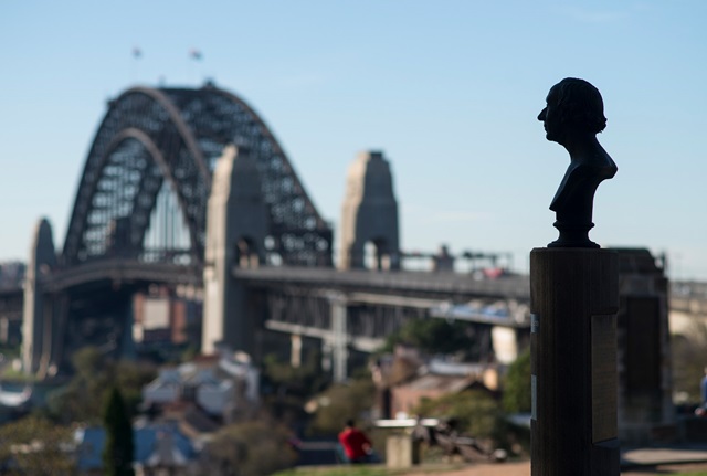 A bronze bust of Danish author Hans Christian Andersen mounted on a sandstone plinth set against a backdrop of the Sydney Harbour Bridge