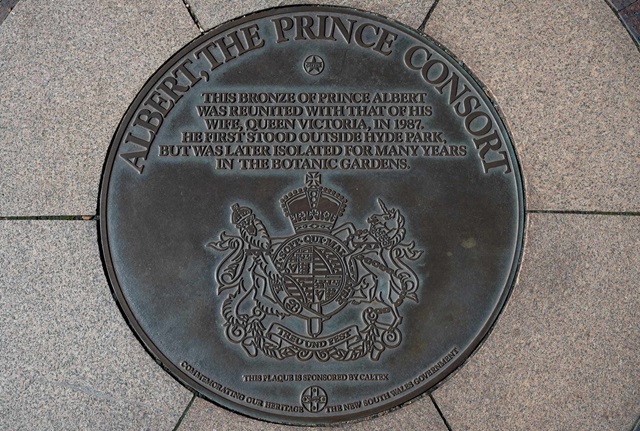 A circular bronze plaque reading "Albert, the Prince Consort. This bronze of Prince Albert was reunited with that of his wife, Queen Victoria, in 1987. He first stood outside Hyde Park, but was later isolated for many years in the botanic gardens." There is an engraved seal below the text.