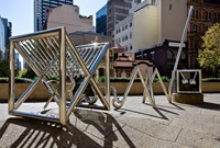 Large stainless-steel sculpture made from tubular pieces with a city skyline in the background