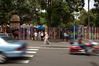 Main road with cars and bikes going past a frontage of a school with a highly coloured metal school fence.