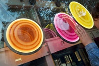 3 large, pendulum discs of coloured acrylic in pink, orange and yellow behind a large window. A child's hand hovers over the pink disc.
