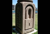 Granite sculpture with padlock carved on one side sitting on a square concrete base in a park.