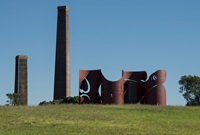 Green parklands with abstract iron sculpture in the distance and large chimney stacks in the background