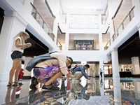 Two people squatting on the glass floor inside Customs House to take pictures of the city model.  Behind the two people, one person takes photo standing on the glass floor. 