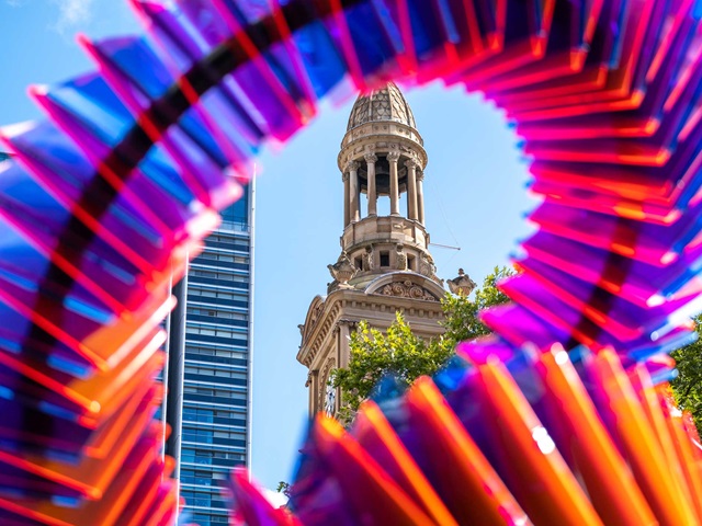 A heritage building's tower and an office building are glimpsed through a swirling purple, blue and orange artwork.