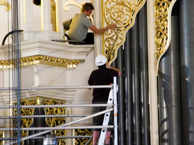 Workmen restoring a part of an ornate organ pipe casing.