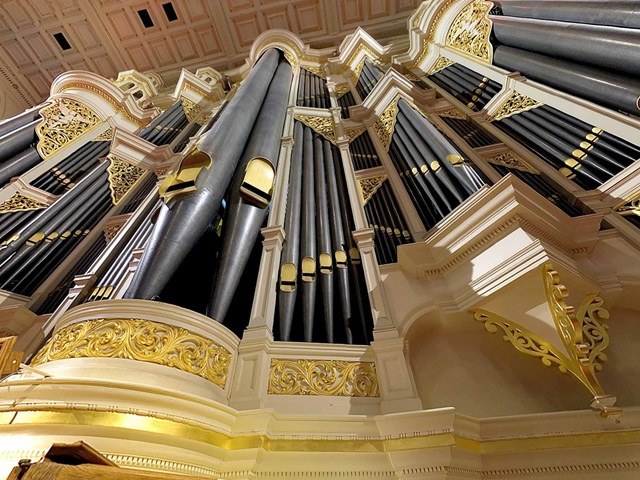 View from below of soaring pipes of an ornate organ.
