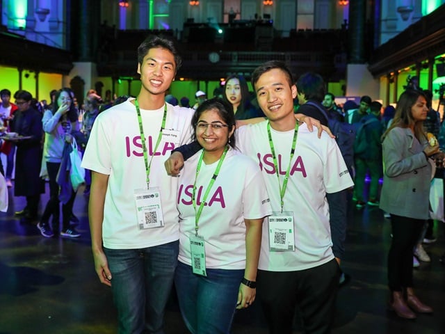 3 students posing for photo with people in the background