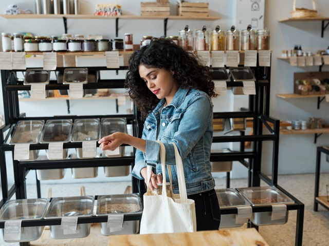 A consumer putting a jar in a reusable bag while shopping at a bulk food store.