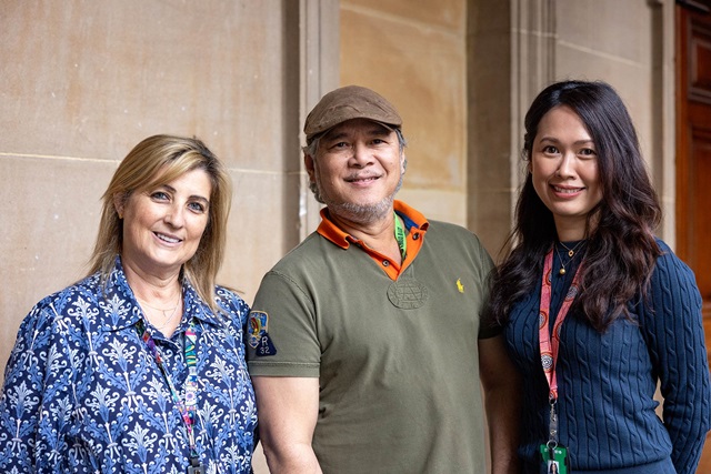 Three City of Sydney employees stand in front of a sandstone building wall, wearing colourful lanyards and smiling.