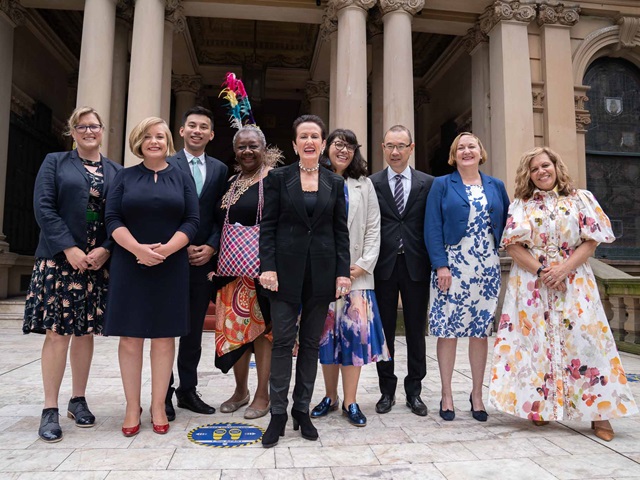 Nine women and men stand in front of a heritage columned building.