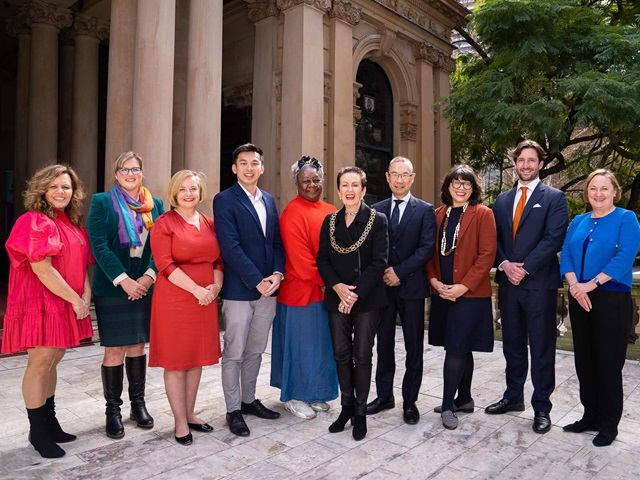 Ten women and men stand in front of a heritage columned building.