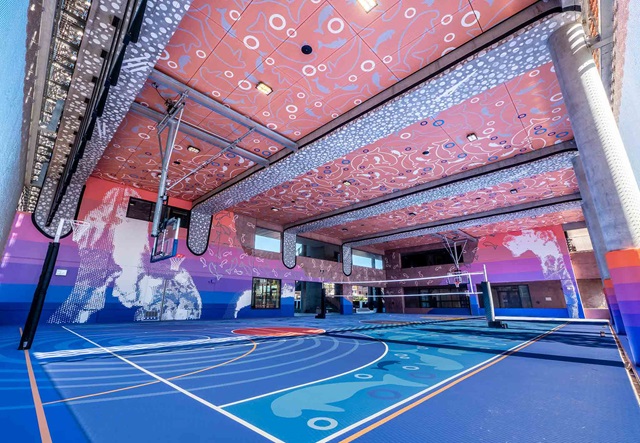 Indoor basketball court with vibrant, abstract artwork covering the walls, ceiling, and floor; basketball hoops and volleyball net are visible.