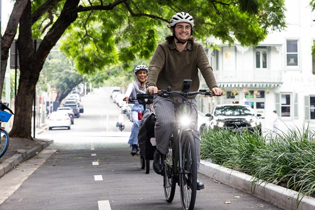 2 people riding bikes down a cycleway in on suburban tree lined street