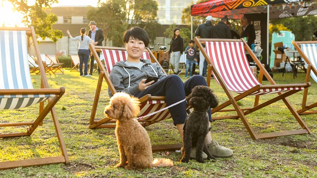 woman sitting on stripy deckchair with 2 small dogs beside her