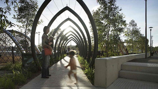 A woman with 2 small children enter a park through a decorative archway
