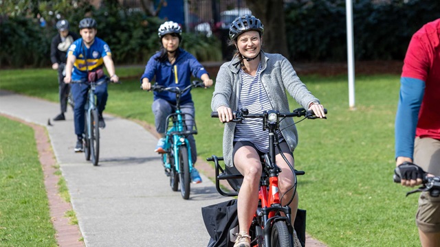 5 people riding on bikes along a cycle path through a park