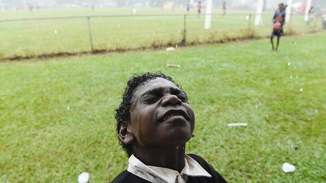 Young boy feels rain on his face at the footy with closed eyes