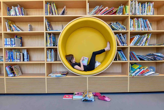 A child reads a book in a library. The yellow seat is circular and set into the bookcase.