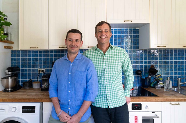 Two men are pictured in their kitchen.
