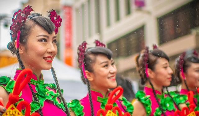 Line of Chinese Festival performers smiling and standing outdoors, dressed in traditional costume.