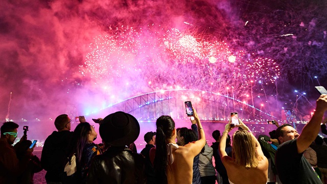 Crowds of people stand and watch pink fireworks explode over the Sydney Harbour Bridge