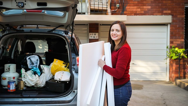 Woman places recycling into the back on a car on a driveway