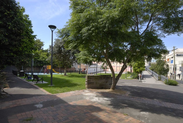 Entrance to park with pathway on the left and grassed area with a children's playground.